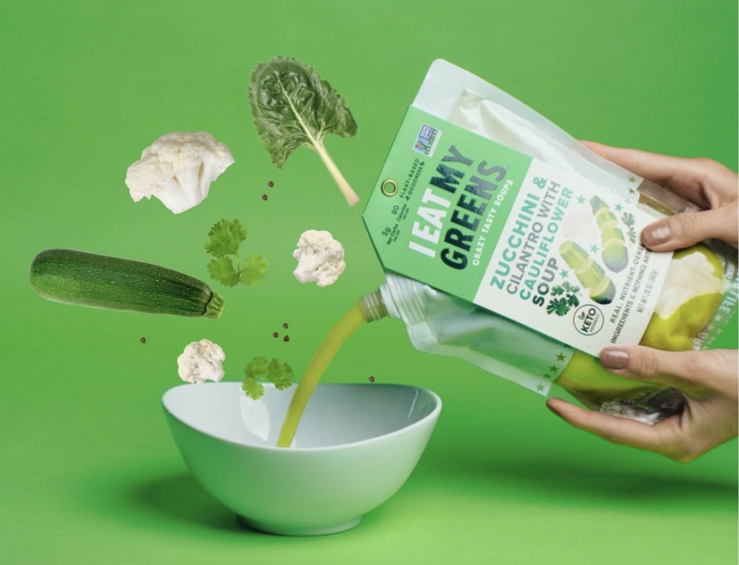 Zucchini & Cauliflower soup pouring into a bowl with fresh ingredients in motion.